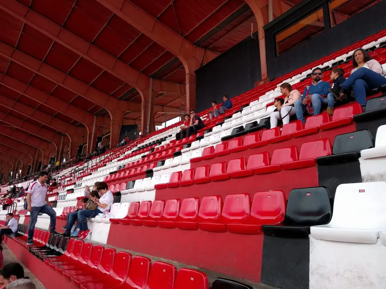 Widok na trybuny stadionu Sevilla. Czerwono-białe siedzenia wypełniają się kibicami, gotowymi na emocje.
