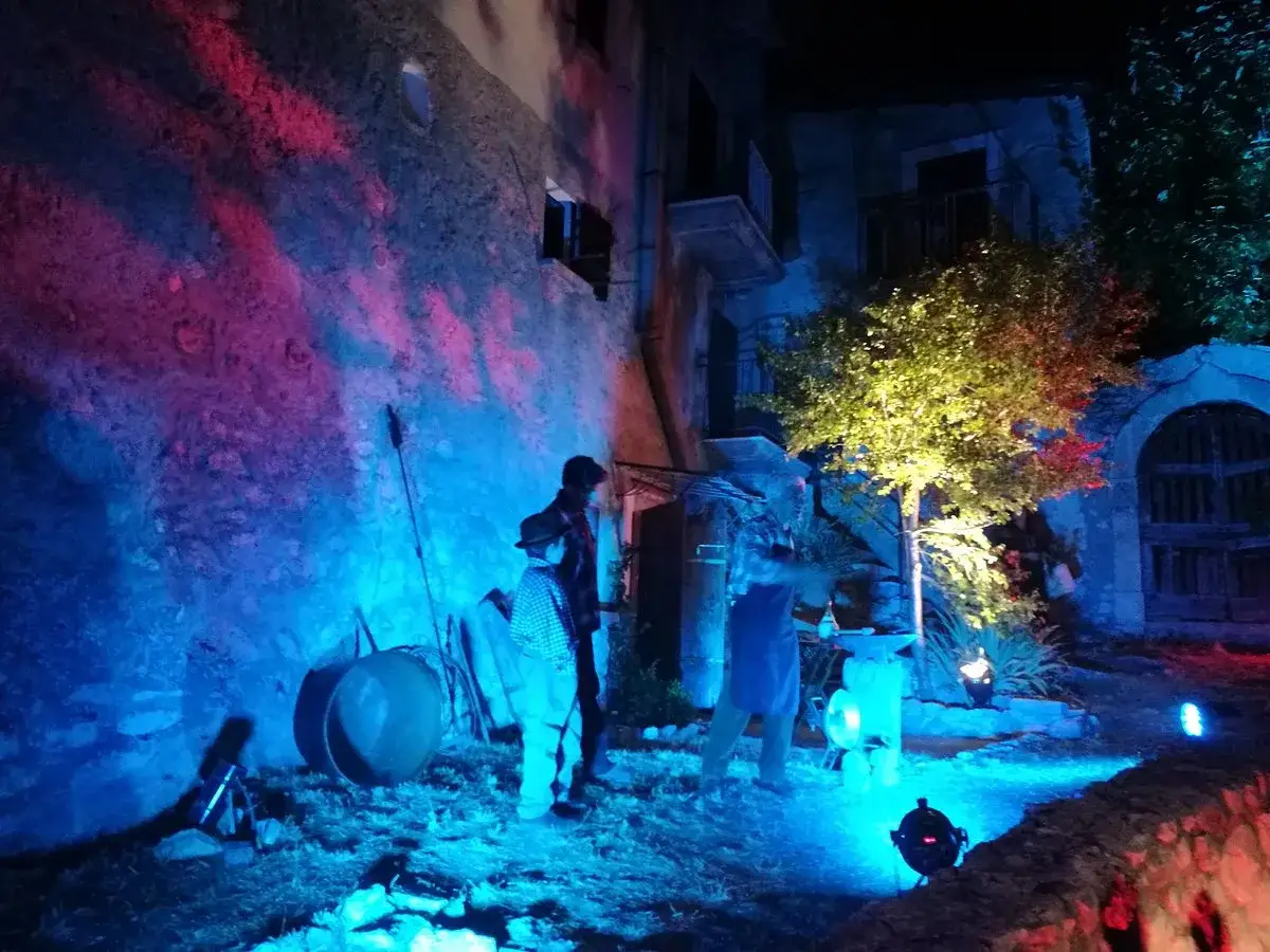 Scena suggestiva per la festa delle streghe in Abruzzo: luci blu e rosa illuminano un antico borgo, con figure misteriose e un albero incantato.