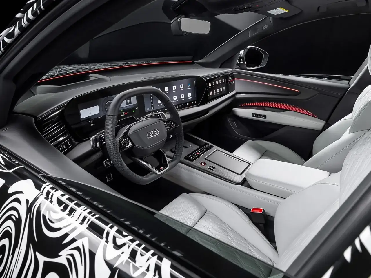 Interni lussuosi dell'Audi Q9 con sedili in pelle chiara, cruscotto digitale e illuminazione d'ambiente rossa.