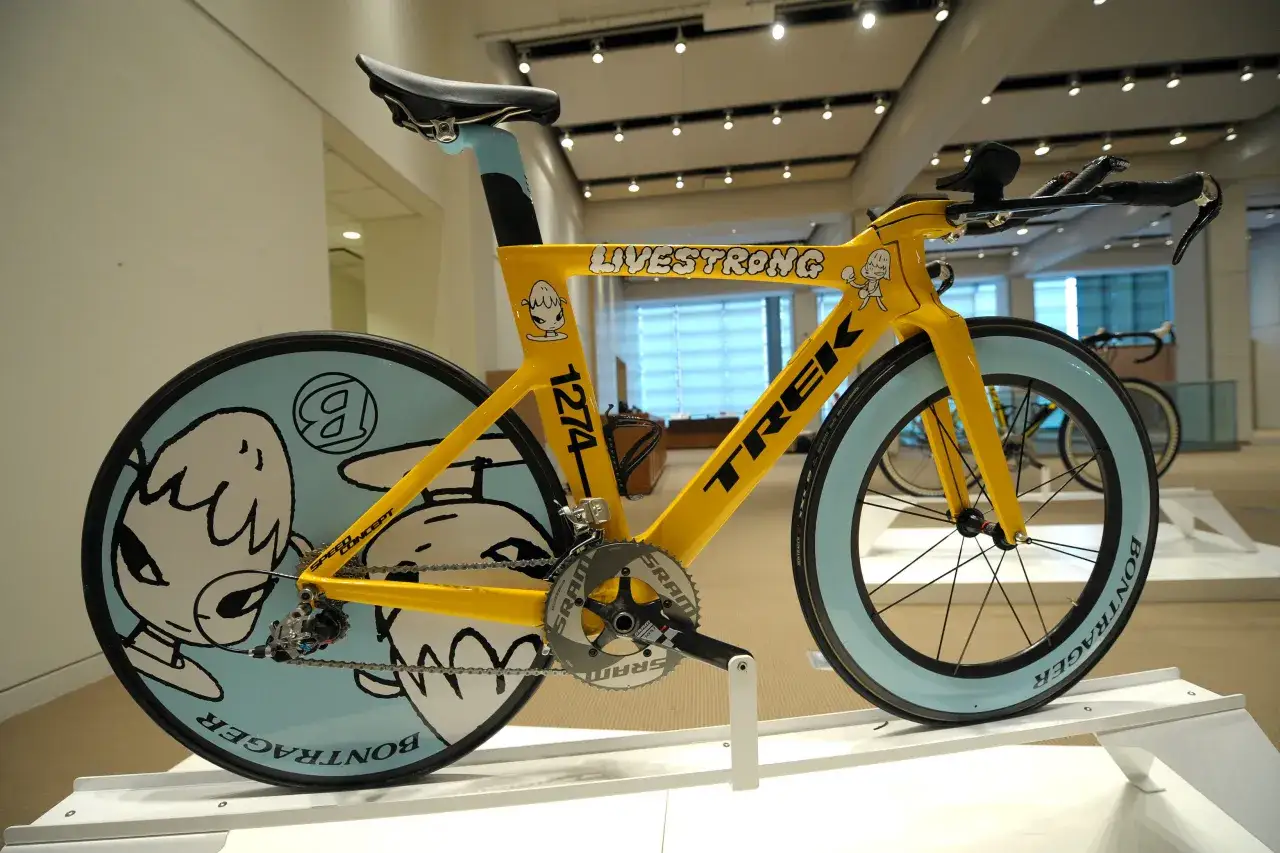Żółty rower wyścigowy TREK z napisem LIVESTRONG i grafiką postaci. To najdroższy rower na świecie, prezentowany na wystawie.