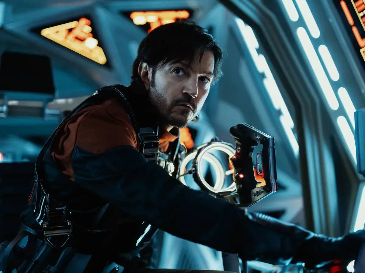 Cassian Andor, con su mirada intensa, se prepara para la acción en la **Andor temporada 3**. Sostiene un dispositivo futurista en una nave.