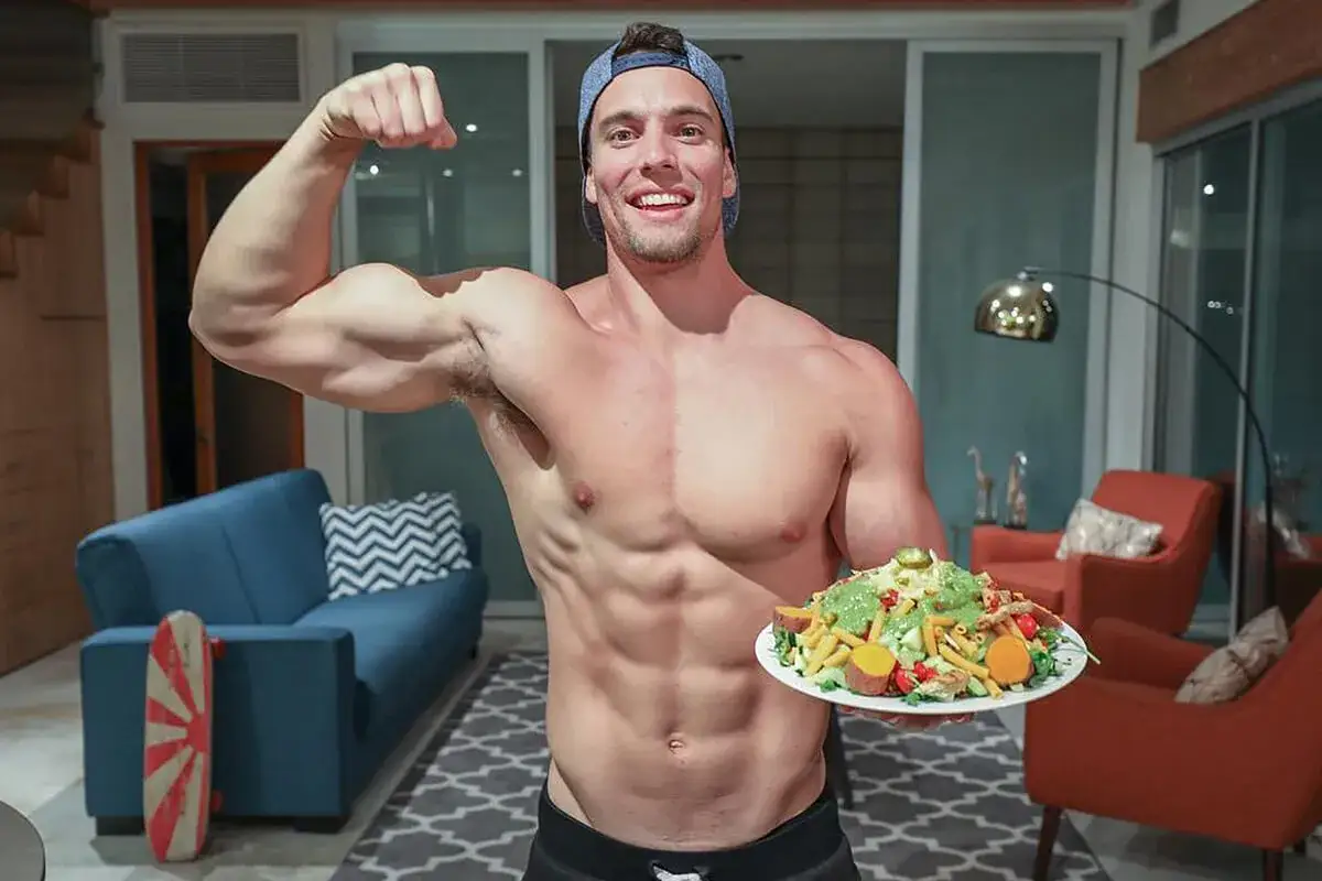 Muskul&ouml;ser Mann zeigt Bizeps und eine gesunde vegane Mahlzeit. Beweis f&uuml;r erfolgreichen vegan Muskelaufbau.