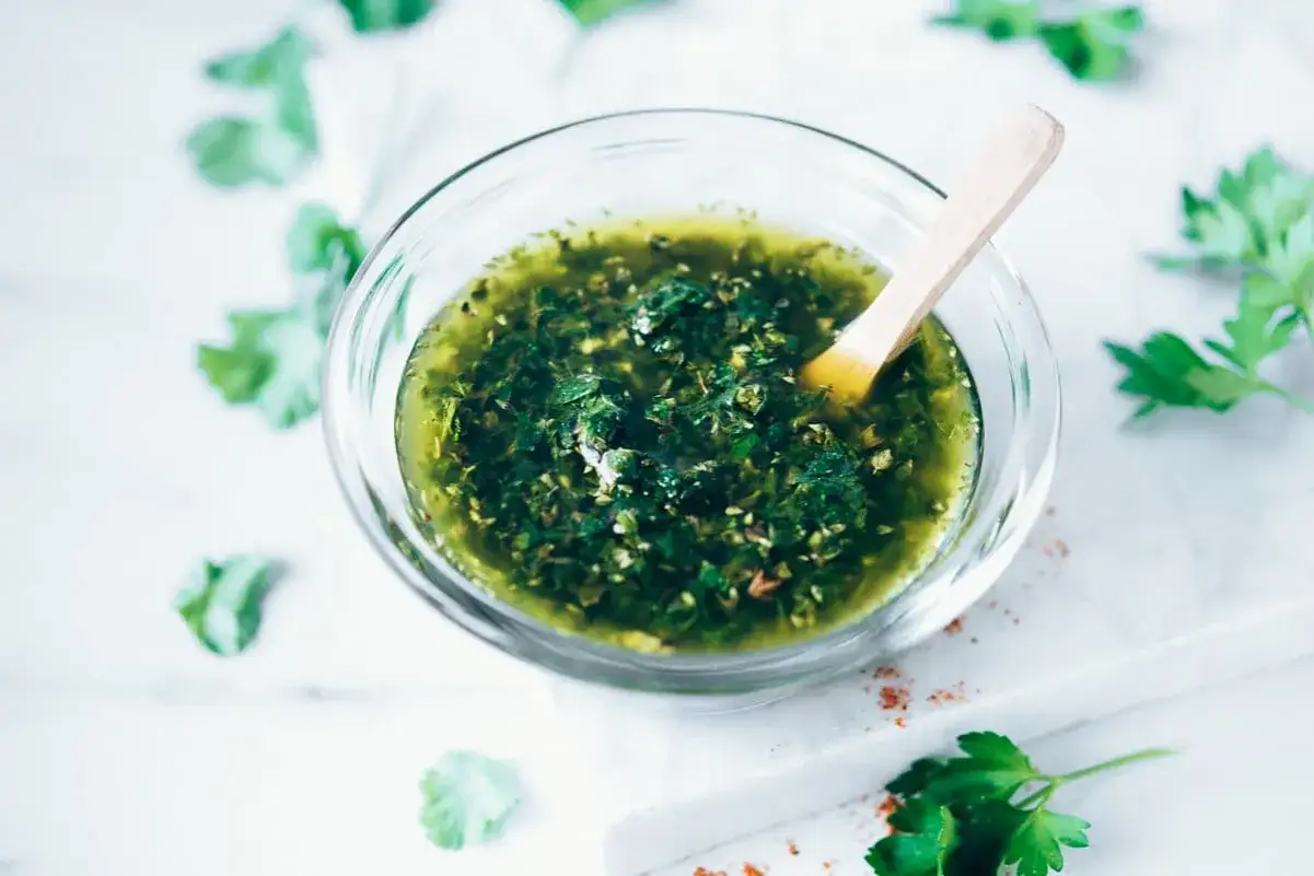 Un tazón de chimichurri fresco, con sus vibrantes chimichurri ingredientes como perejil y ajo, listo para realzar cualquier plato.
