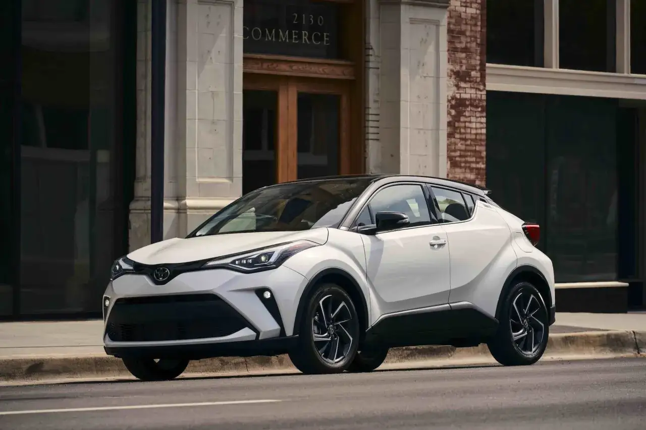 Biała Toyota C-HR 2022 z czarnym dachem zaparkowana przed budynkiem z napisem 