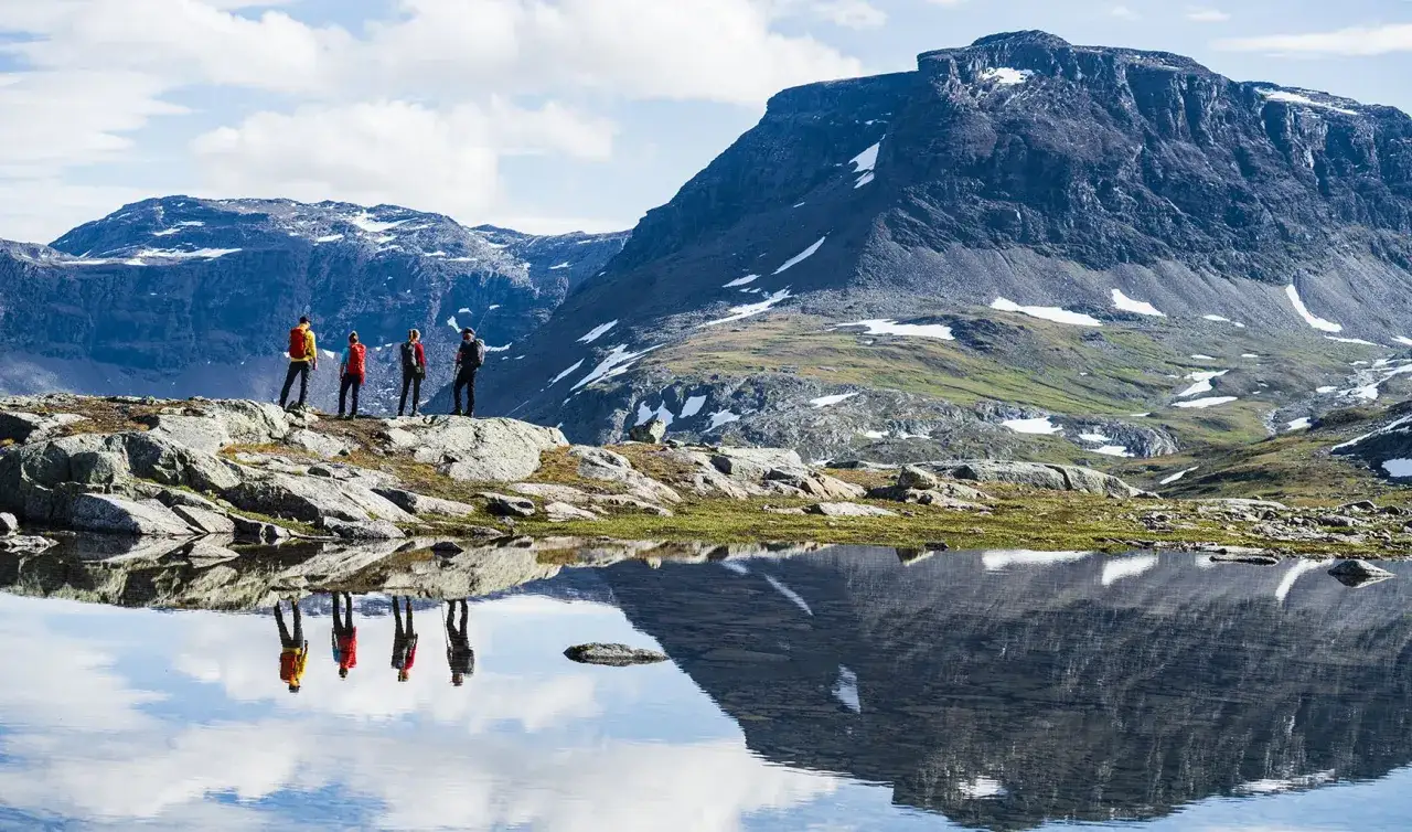 Vandrare njuter av midnattssol Sverige vid en spegelblank sj&ouml; med berg i bakgrunden.
