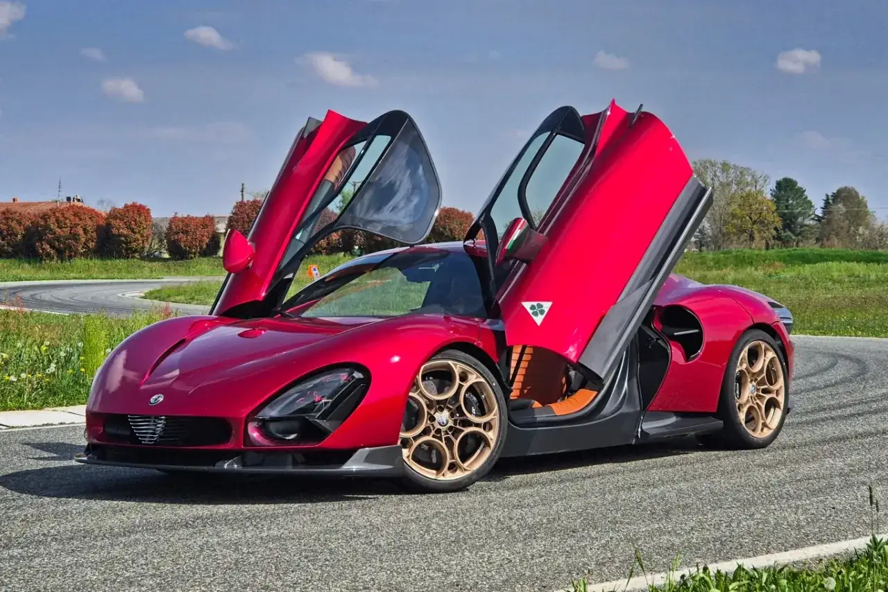 Czerwone Alfa Romeo 33 z otwartymi drzwiami typu gullwing na torze wyścigowym.