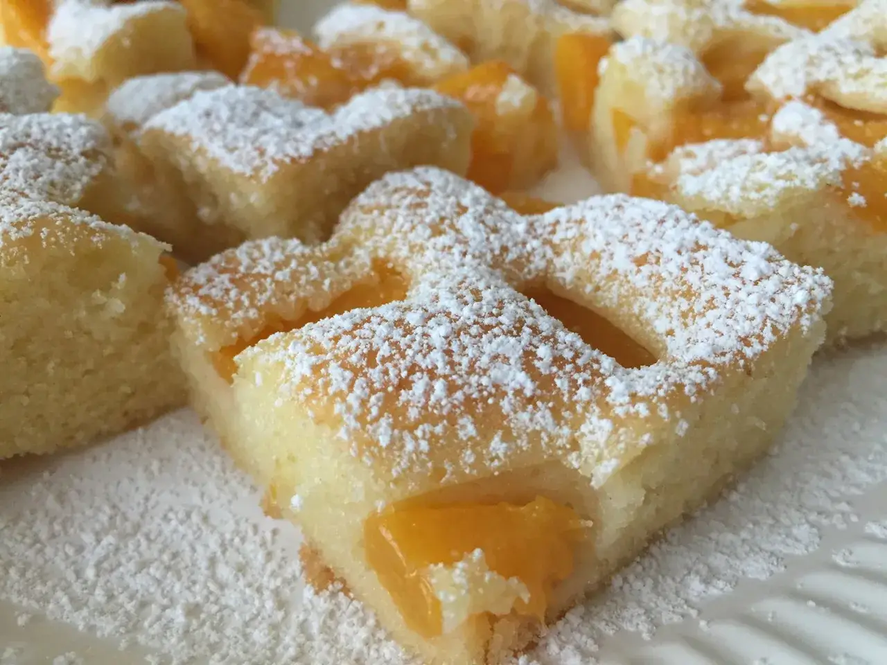 Saftiger Pfirsich Blechkuchen mit Vanillepudding, bestäubt mit Puderzucker. Ein süßer Genuss!