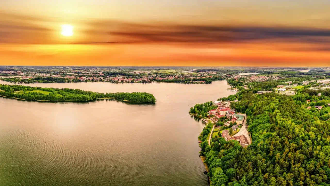 Widok z wieży widokowej na Mazurach: jezioro, lasy i miasteczko o zachodzie słońca.