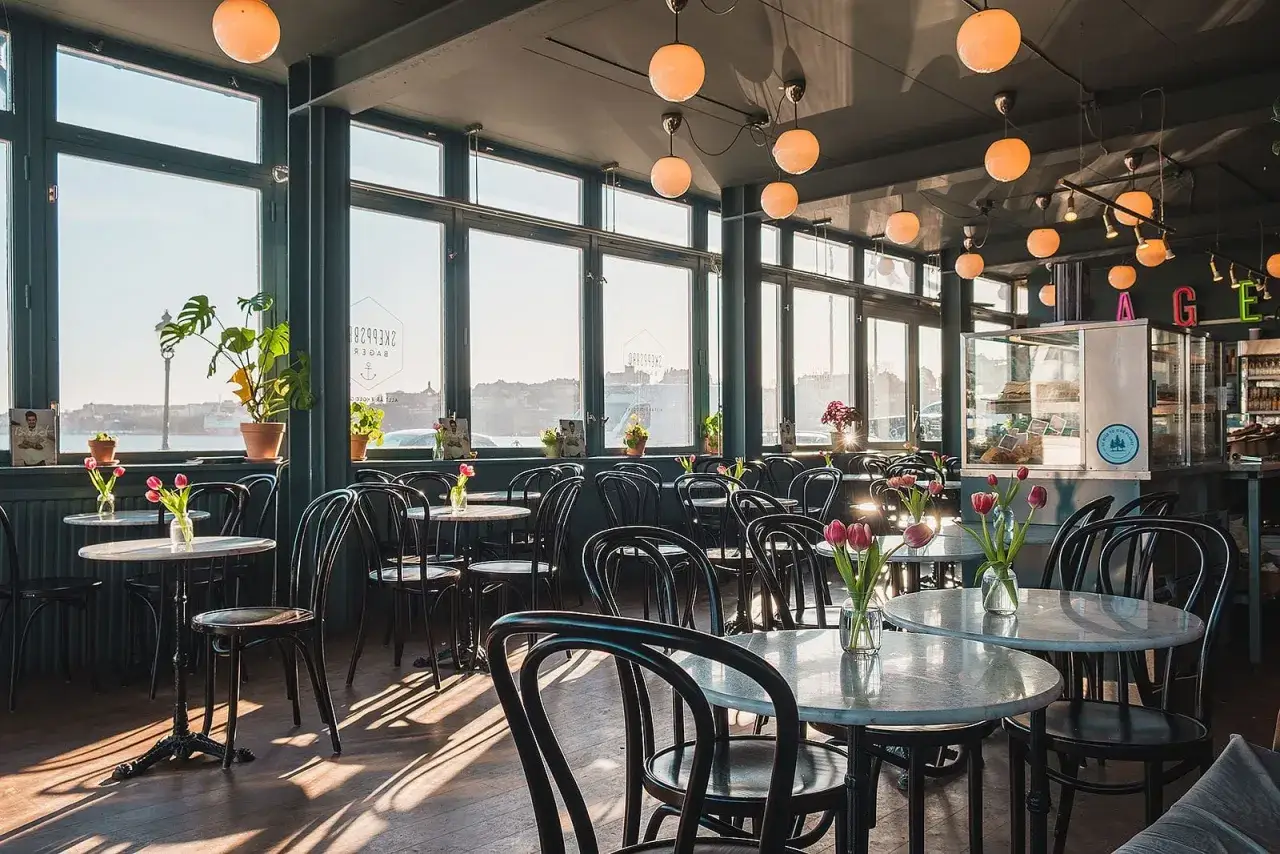 Mysig lokal med m&aring;nga bord och stolar, perfekt f&ouml;r en fika i Gamla Stan. Solen strilar in genom de stora f&ouml;nstren.
