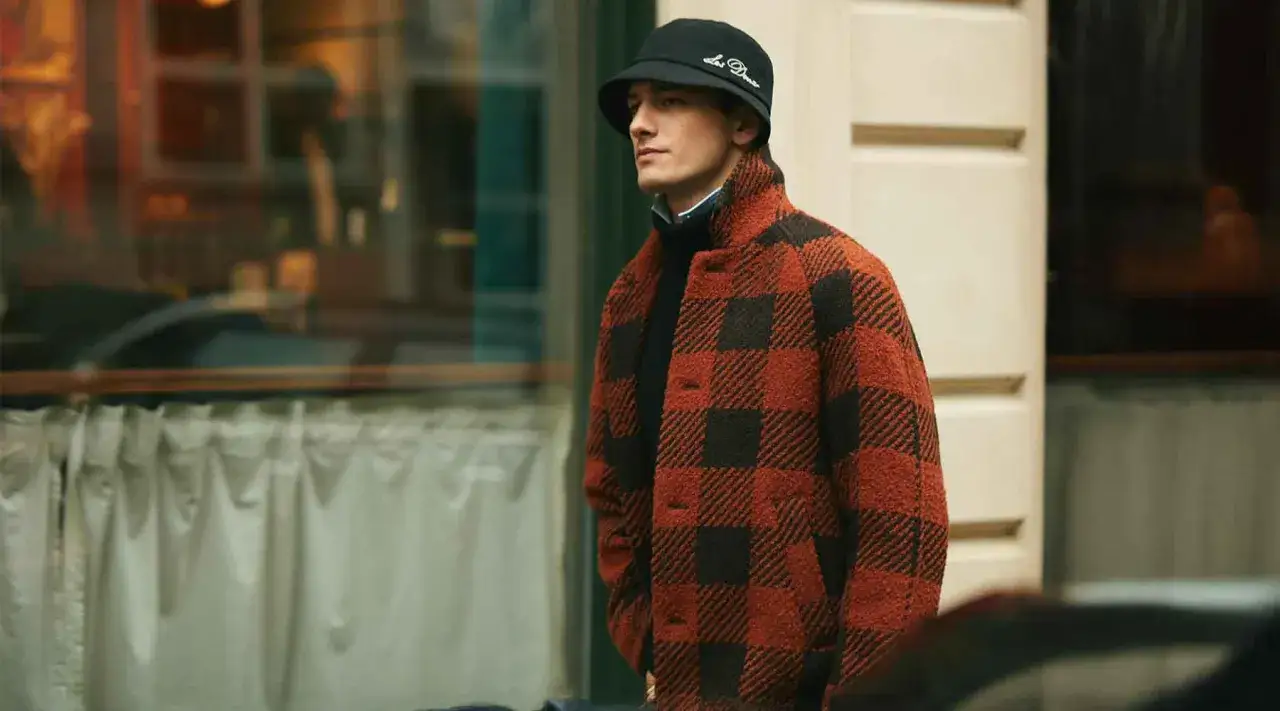 Mann im karierten Jackett und Fischerhut, ein Look im **mode 90er jahre** Stil, steht vor einem Schaufenster.