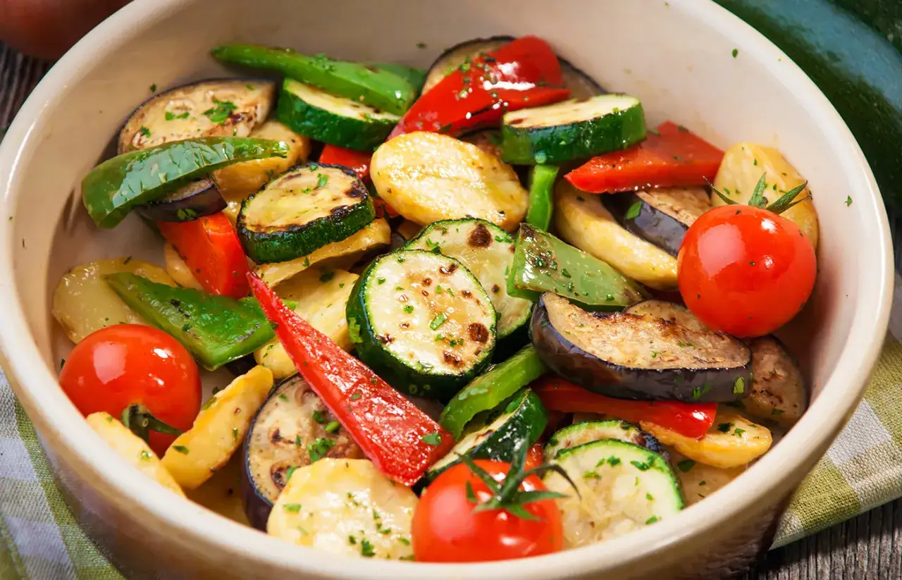 Un colorido panache de verduras asadas, con rodajas de calabacín, berenjena, pimientos y tomates cherry, espolvoreado con perejil fresco.