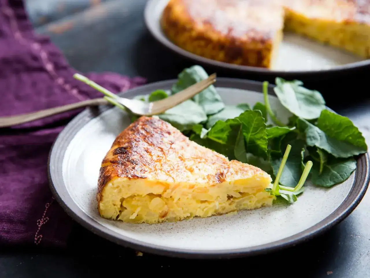 Ein St&uuml;ck spanische Tortilla, ein klassisches Gericht aus Eiern und Kartoffeln, serviert mit frischem Gr&uuml;n. Perfekt f&uuml;r Eier Rezepte!
