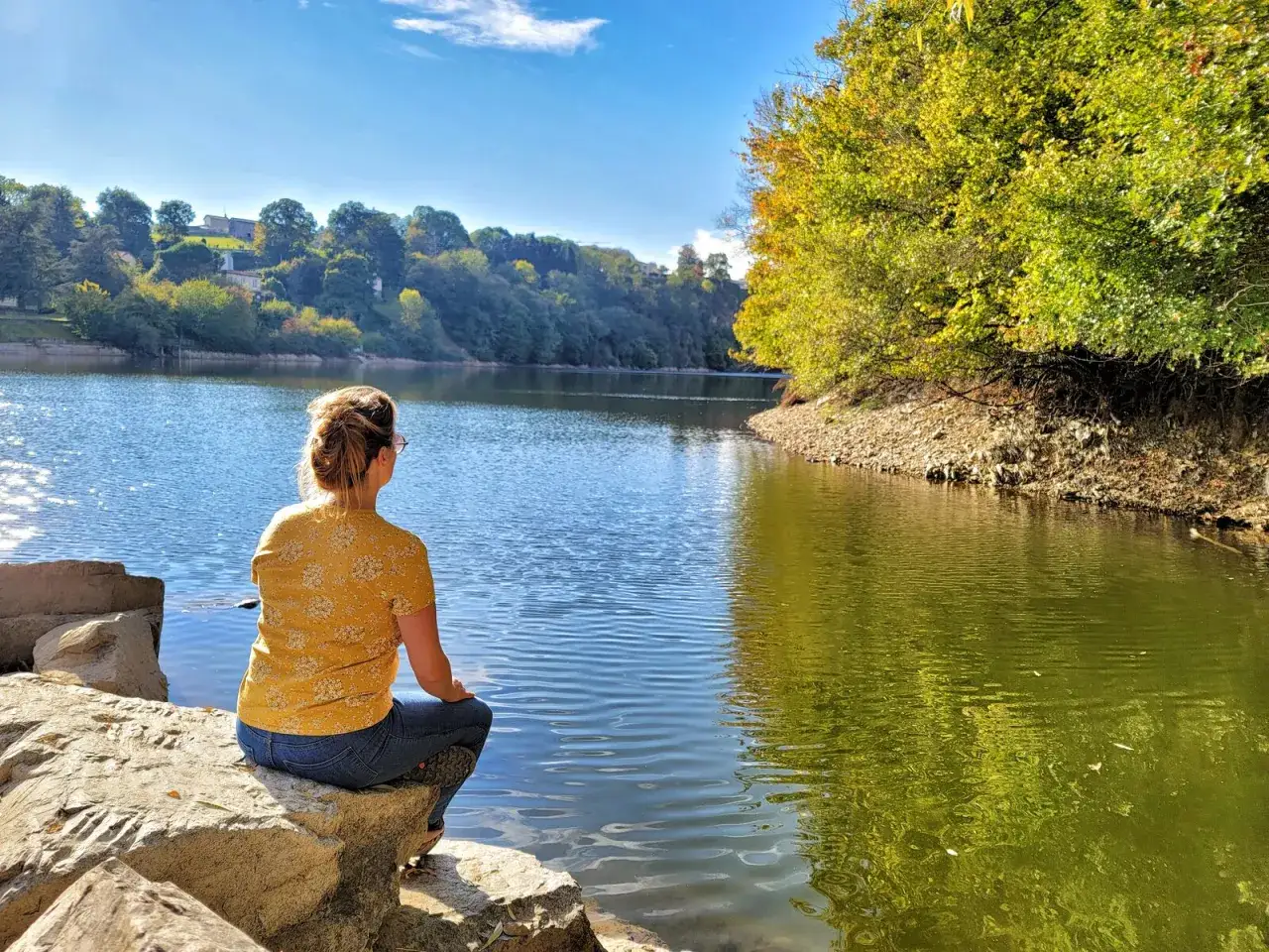 Une femme assise sur des rochers admire le lac, un bel itin&eacute;raire dans la for&ecirc;t de Mervent.