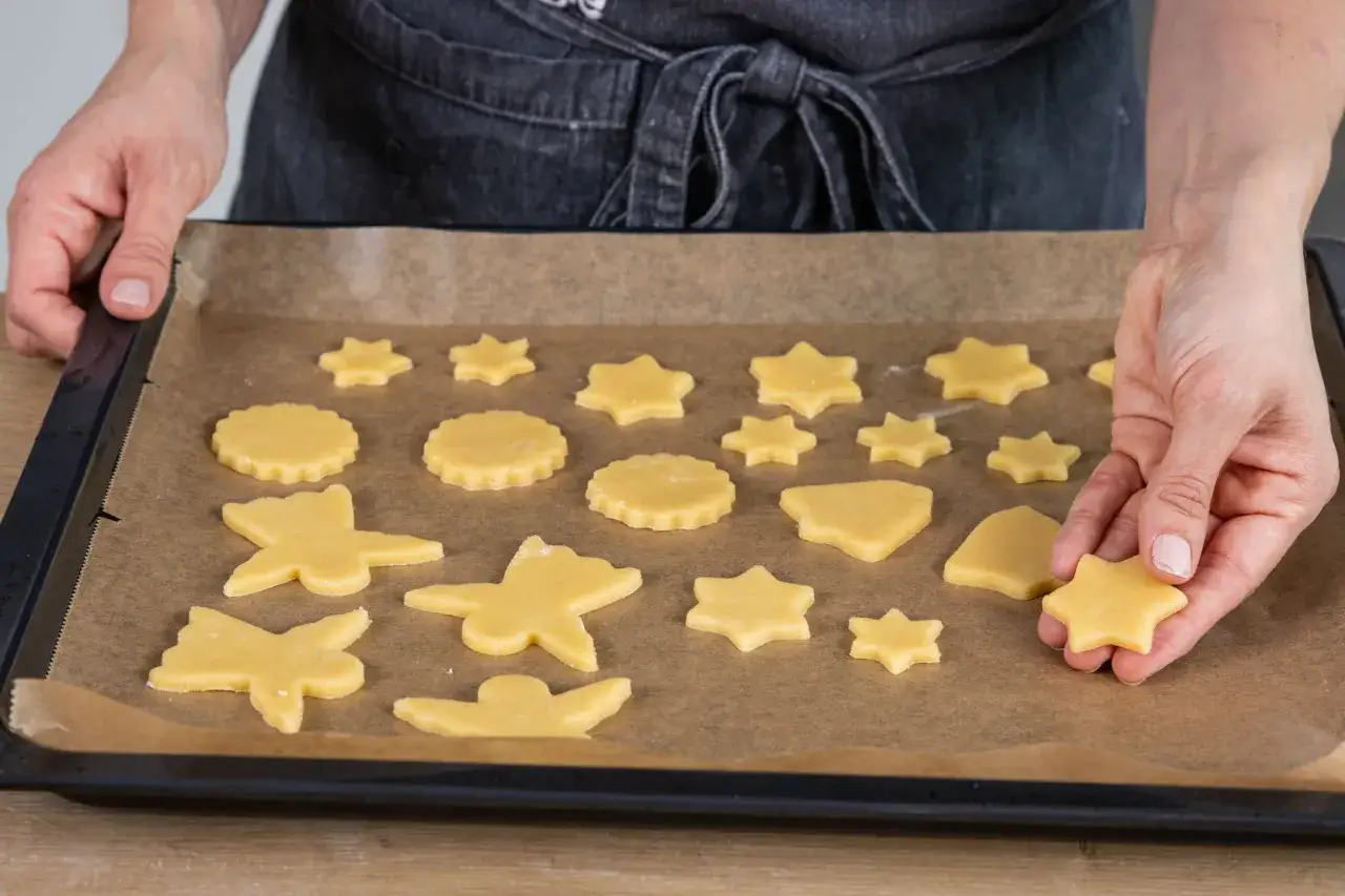 H&auml;nde legen Sterne, Schmetterlinge und Kreise aus Teig zum Kekse backen auf ein Backblech.