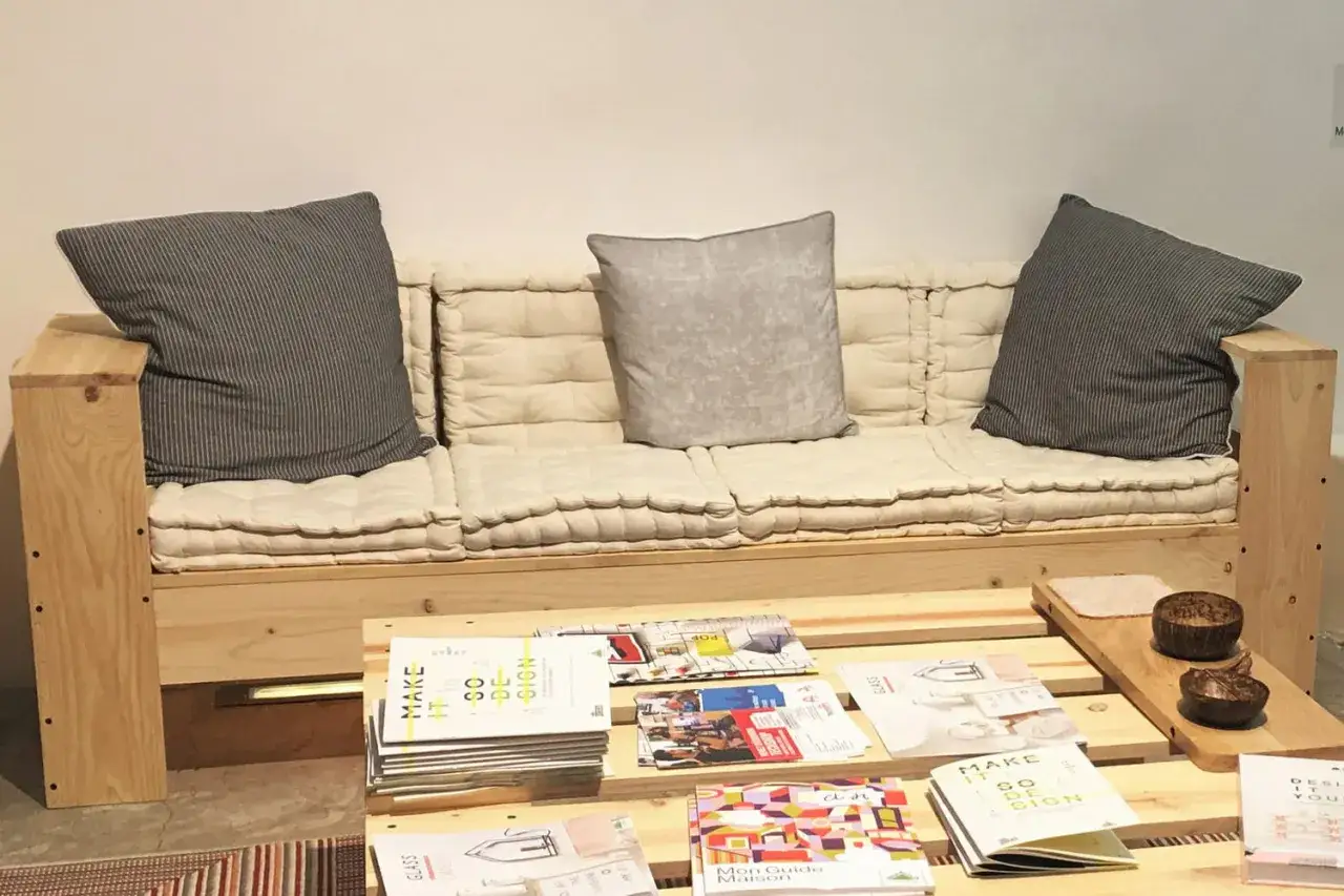 Canapé en palette plan, confortable avec coussins beiges et gris. Une table basse en palettes présente des magazines de design.