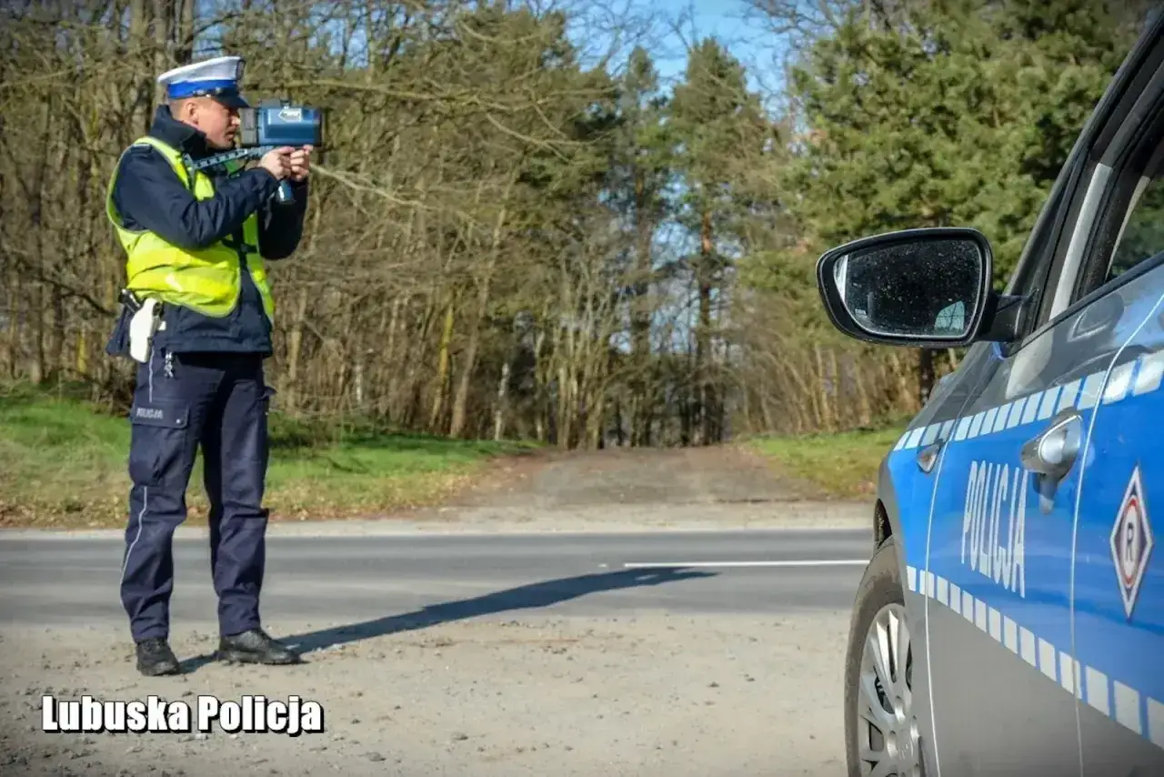Policjant mierzy prędkość, aby zapobiec zatrzymaniu prawa jazdy za prędkość. Obok radiowóz.
