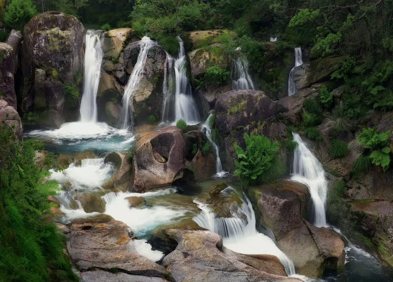 Cascada de Fervenza de Noveira, con múltiples saltos de agua cayendo entre rocas cubiertas de musgo y vegetación exuberante.