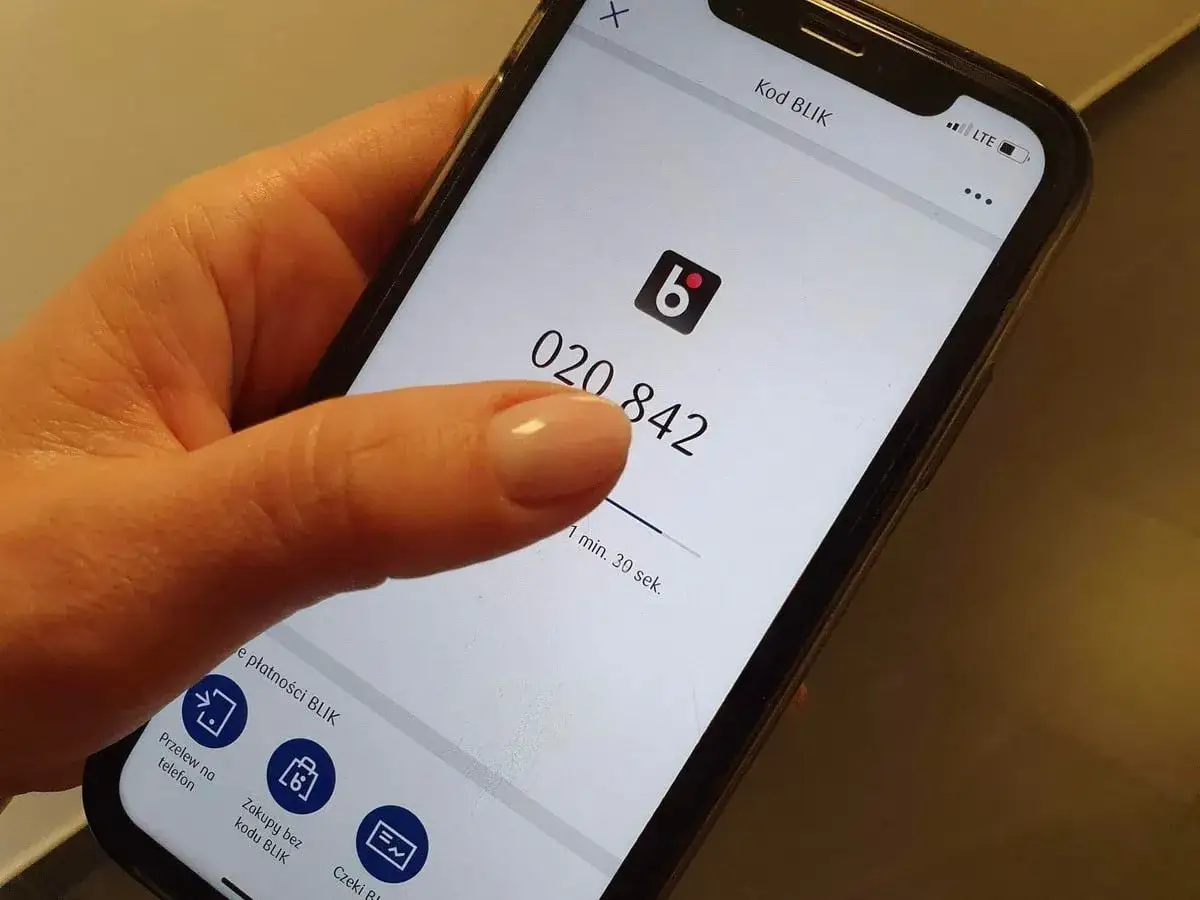 Dłoń pokazuje ekran telefonu z kodem BLIK. Zastanawiasz się, jak cofnąć przelew BLIK na telefon? Sprawdź opcje w aplikacji.