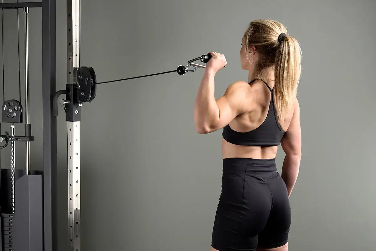 Kvinna tr&auml;nar axlar p&aring; gym med kabelmaskin. Starka muskler syns tydligt.