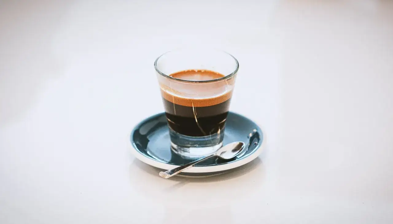 Ein doppelter Espresso, italienisch, mit Crema, auf einem kleinen Teller mit L&ouml;ffel.
