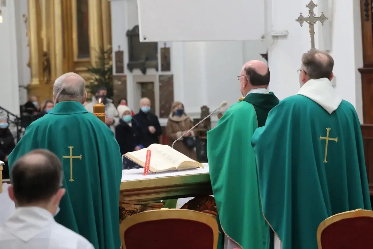 Jak zachować się na pierwszej mszy świętej? Poradnik dla gości. Trzech księży w zielonych szatach, otwarty brewiarz, świeca i wierni w kościele.