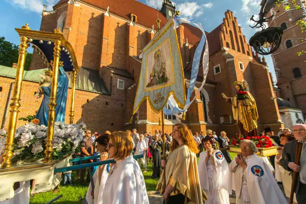 Prozession mit Marienstatue und Fahne vor einer Kirche. Menschen in weißen Gewändern, ein Festtag in Polen.