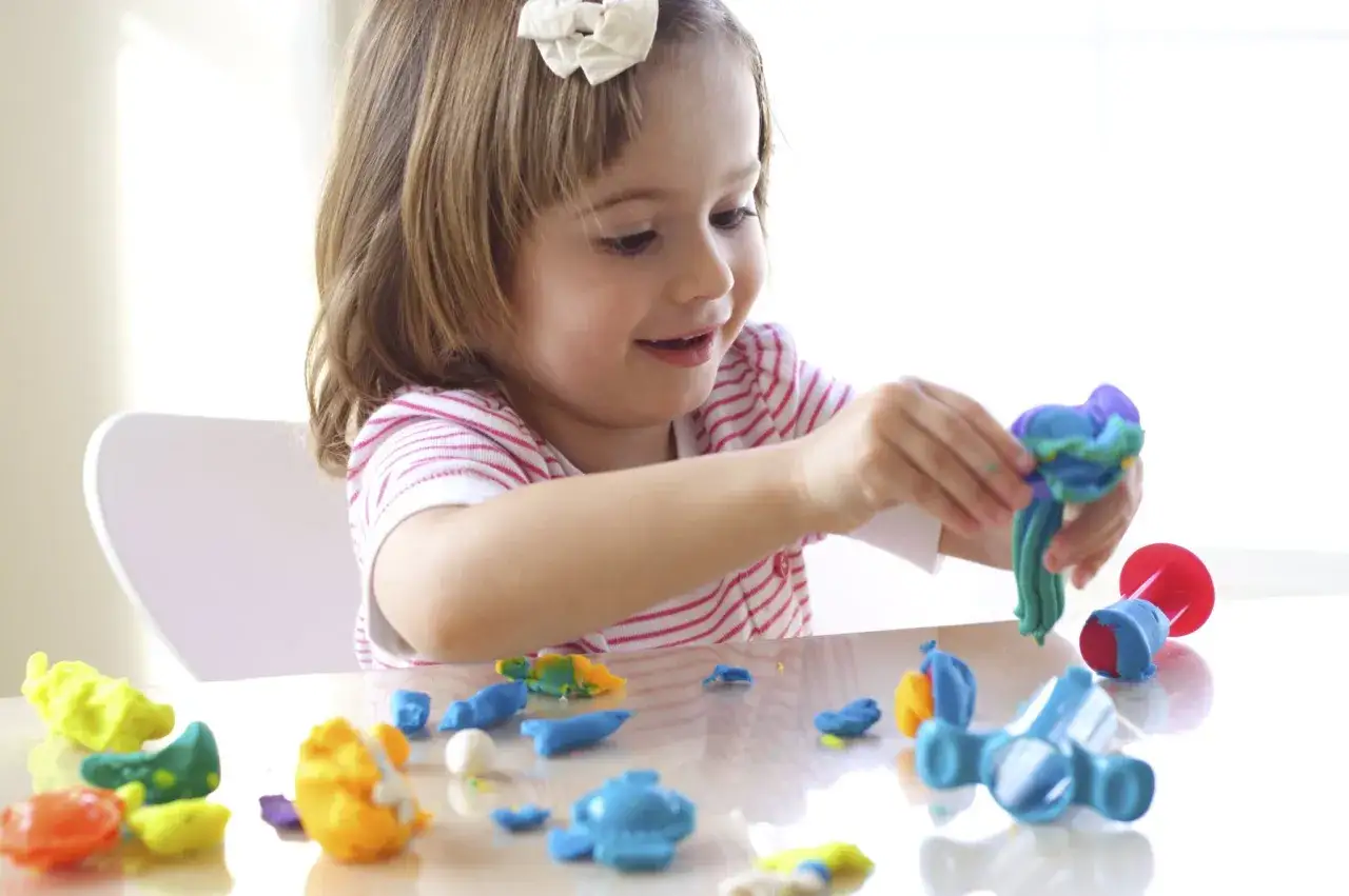Ni&ntilde;a sonriente crea figuras con plastilina, disfrutando de juegos creativos.