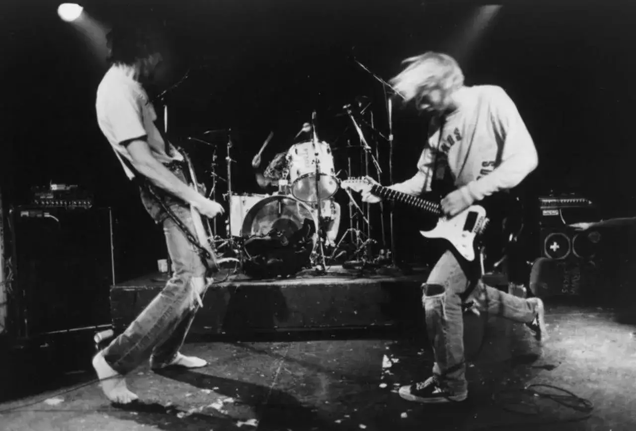 Nirvana grając swoje utwory na żywo. Kurt Cobain szaleje z gitarą, basista pochyla się nad instrumentem, a perkusista wybija rytm.