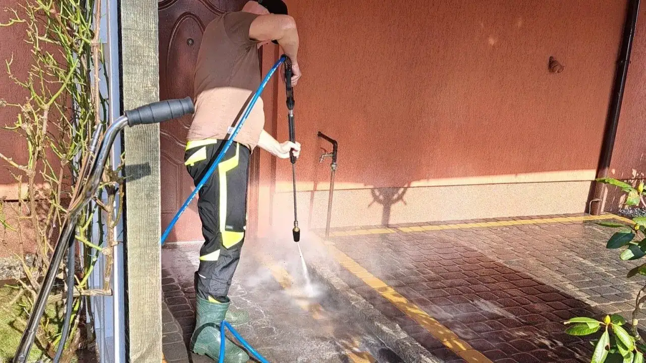 Mężczyzna myjką ciśnieniową usuwa co na mech na kostce brukowej przy drzwiach.