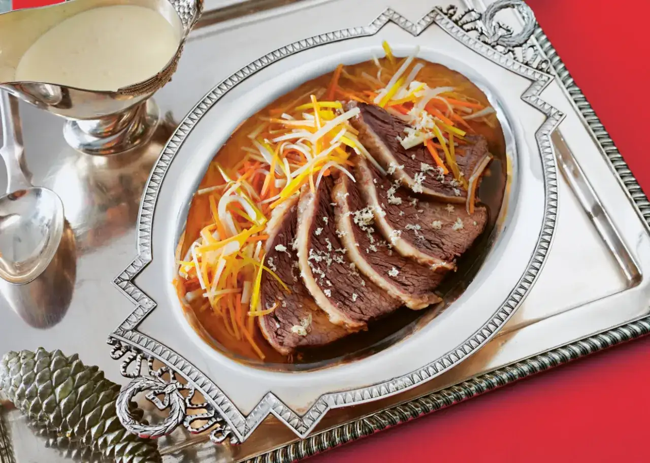 Zart geschnittener Tafelspitz braten im Topf, garniert mit Julienne-Gemüse und einer cremigen Sauce daneben.