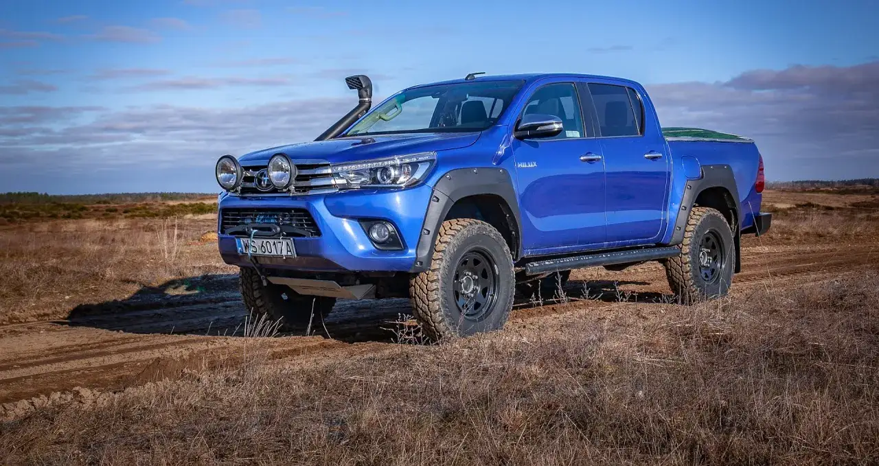 Niebieski Toyota Hilux, terenowy jeep, gotowy na przygodę w suchym krajobrazie.