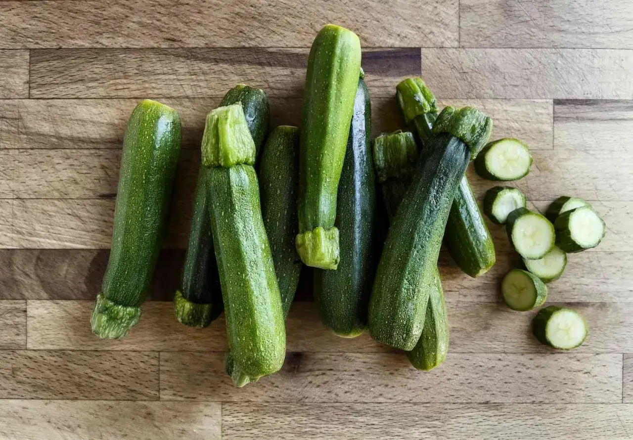Frische Zucchini, bereit, roh gegessen zu werden. Einige sind geschnitten, andere ganz, auf einem Holzhintergrund.