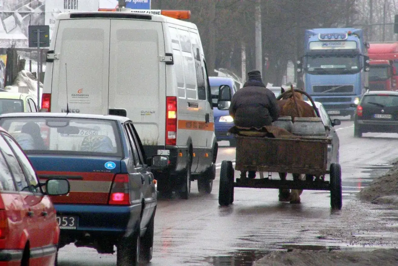Wóz konny z beczkami na mokrej drodze, wyprzedzanie pojazdu wolnobieżnego przez samochody.