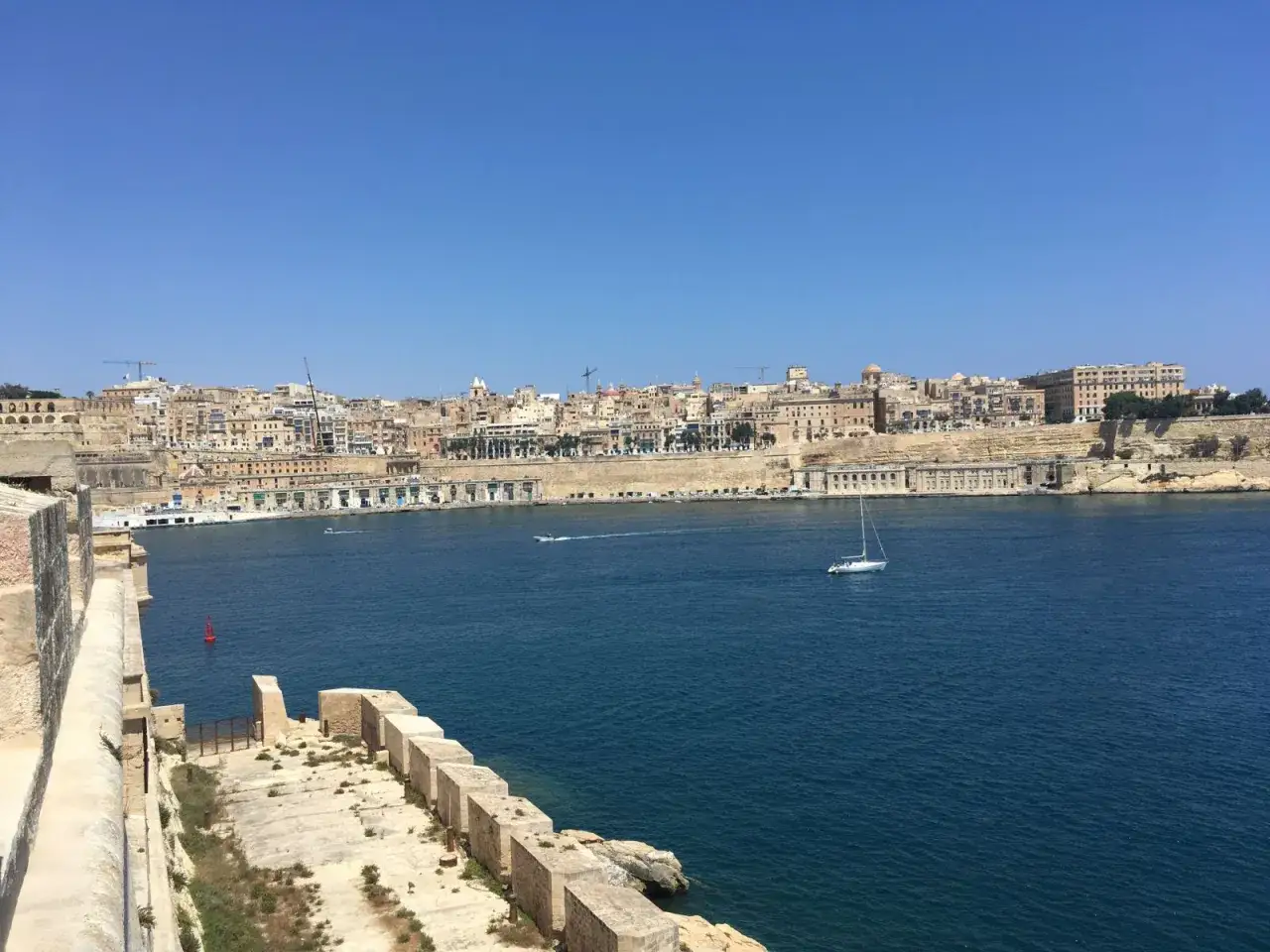 Vue panoramique de La Valette, Malte, avec ses remparts, la mer bleue et un voilier. Un souvenir de séjour à Malte la Valette.