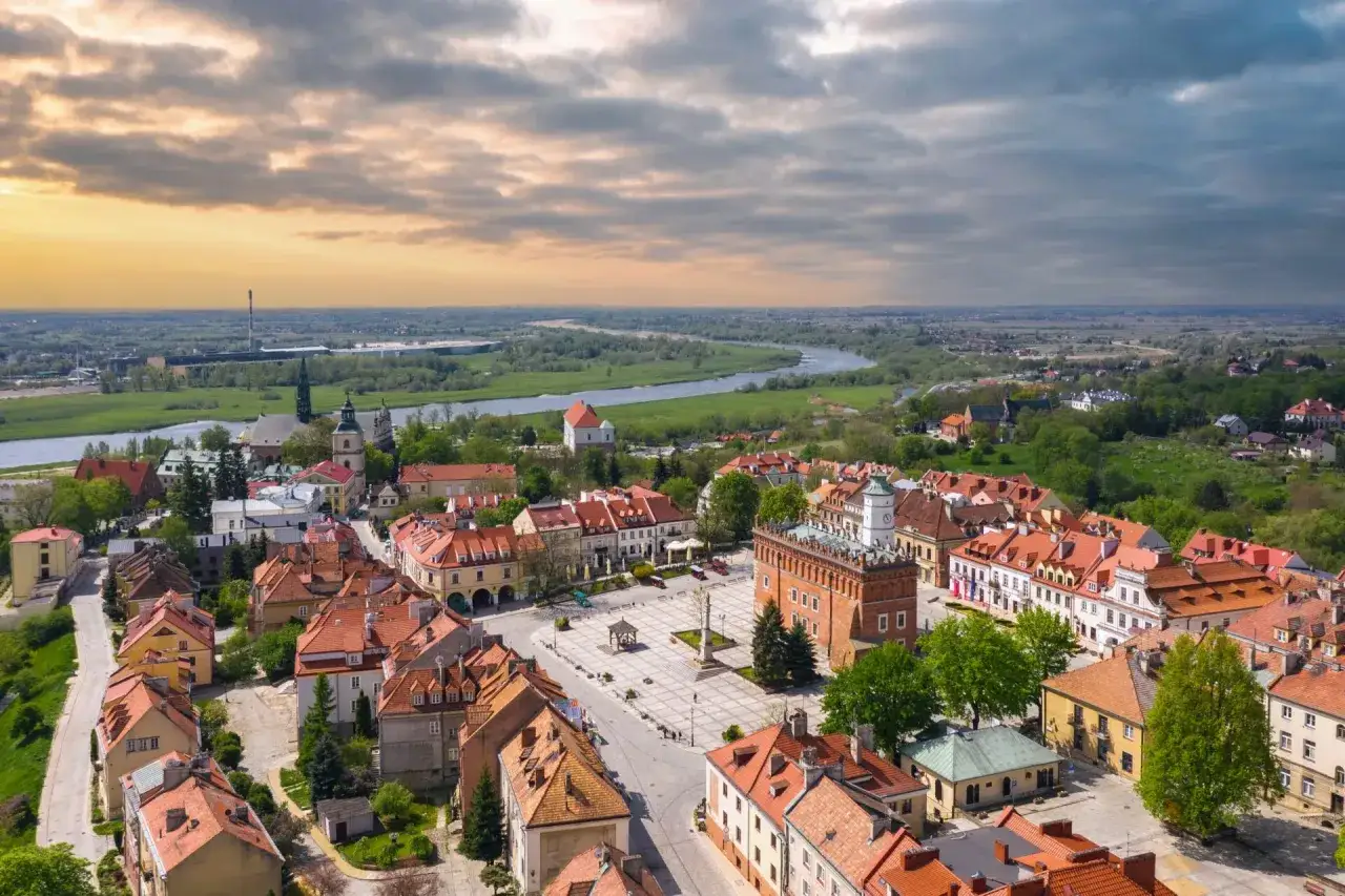 Urokliwy rynek i rzeka w miasteczku zakochanych w Polsce. Dachy kamienic i zieleń tworzą malowniczy krajobraz.