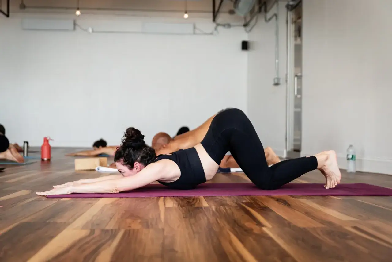 Clase de yoga vinyasa. Mujeres y hombres en postura de perro boca abajo en esterillas moradas. El vinyasa significado es fluidez.