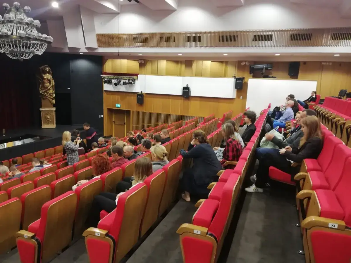 Widownia w operze lubelskiej czeka na rozpoczęcie spektaklu. Czerwone fotele wypełniają widzowie.