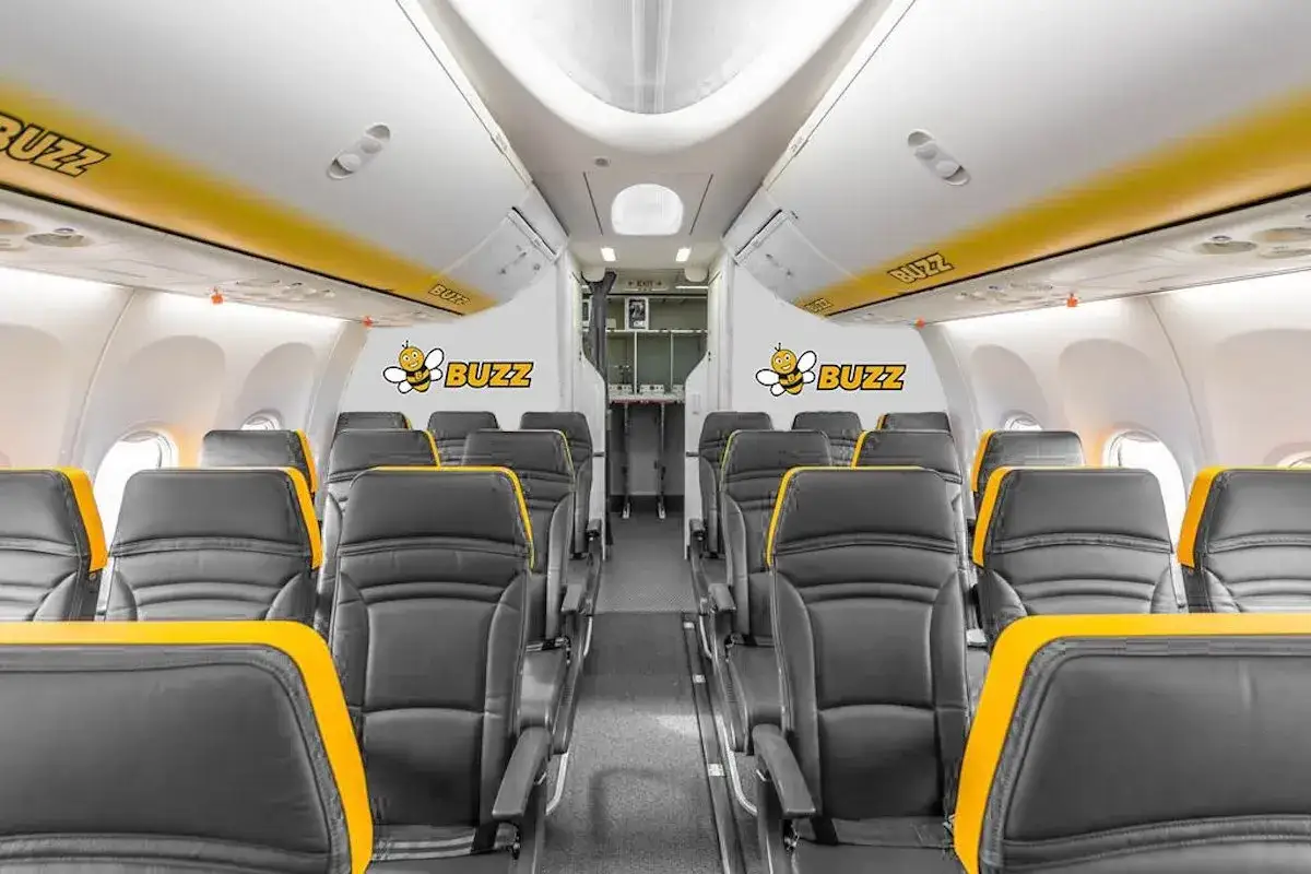 Wnętrze samolotu Buzz, linii lotniczej należącej do Ryanair. Widok na rzędy czarnych foteli z żółtymi akcentami.