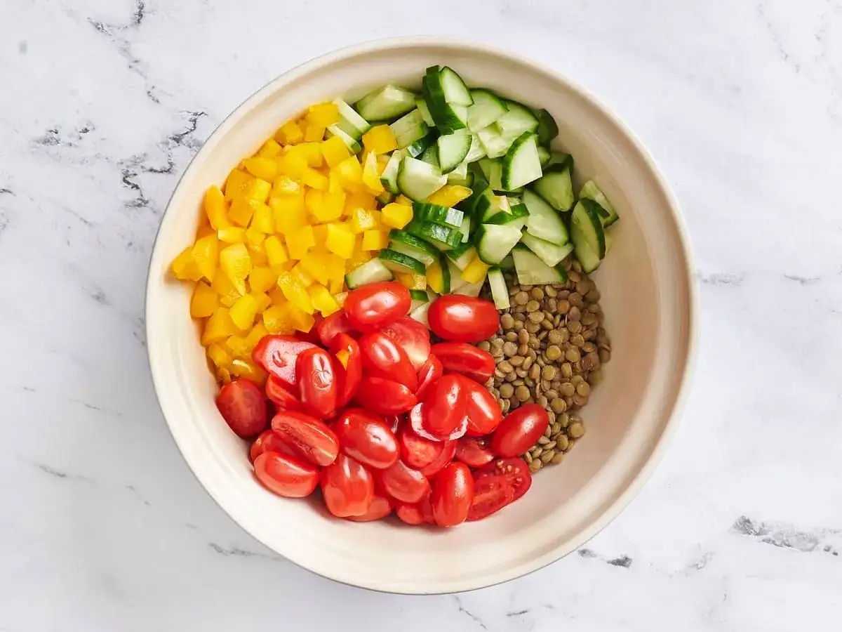 Bunte Zutaten f&uuml;r ein Linsensalat Rezept: gekochte Linsen, Kirschtomaten, gelbe Paprika und Gurkenw&uuml;rfel in einer Sch&uuml;ssel.