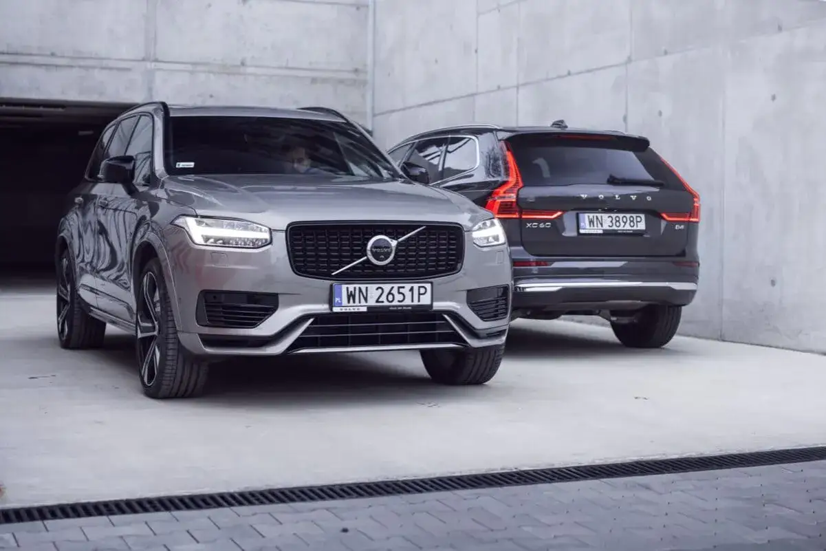 Dwa SUV-y Volvo: szary XC60 T6 z przodu i ciemny XC60 z tyłu, zaparkowane na betonowym podjeździe.