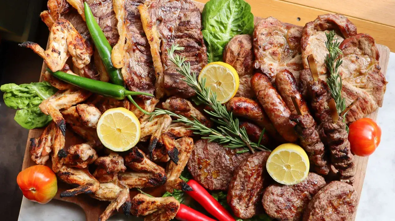 Ein Festmahl für ein italienisch grillen: saftige Steaks, Hähnchenflügel, Würstchen, Spieße, dazu Zitronenspalten, Chilis und Tomaten.