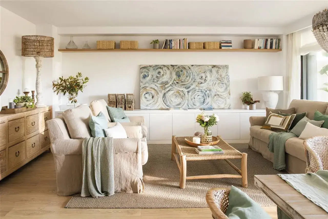 Salón acogedor con sofás de lino, mesa de centro de ratán y cuadros apoyados en muebles bajos.
