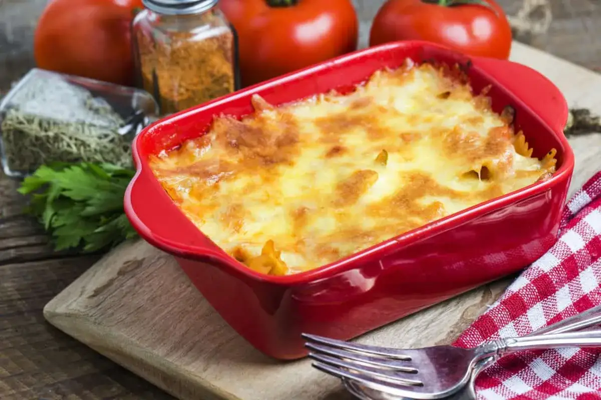 Lasa&ntilde;a de at&uacute;n reci&eacute;n horneada, dorada y burbujeante en un plato rojo, lista para ser servida.