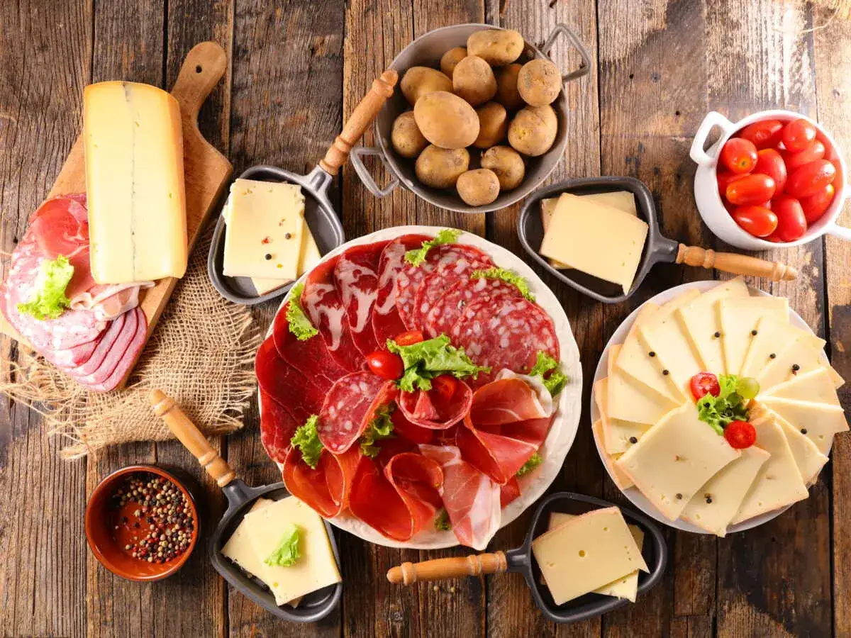 Une variante raclette gourmande : plateau de charcuteries, fromages variés, pommes de terre et tomates cerises, prêt à être dégusté.