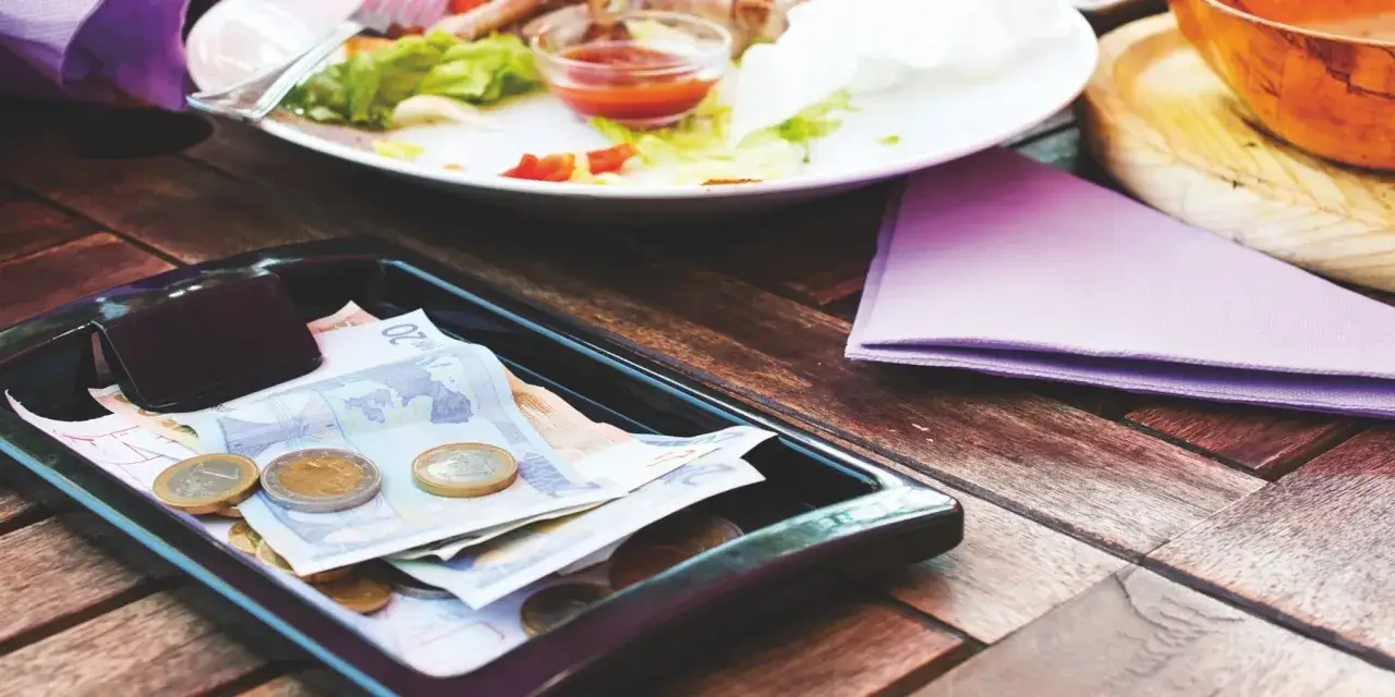 Na tacy leżą banknoty euro i monety, obok talerz z resztkami jedzenia. To rachunek w restauracji po angielsku.