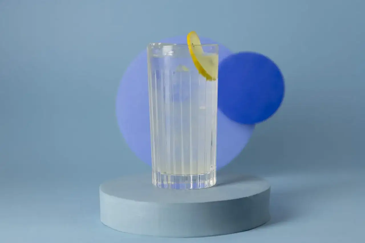 Ein Glas mit Wodka mit Wasser und einer Zitronenscheibe steht auf einem Podest vor blauen Kreisen.