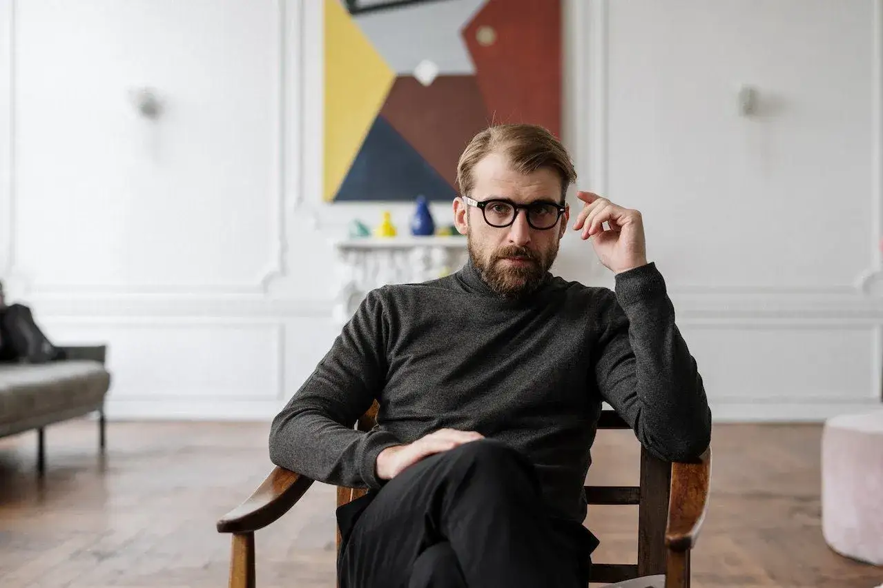 Un homme au visage long, portant des lunettes, réfléchit en s'appuyant sur son doigt.