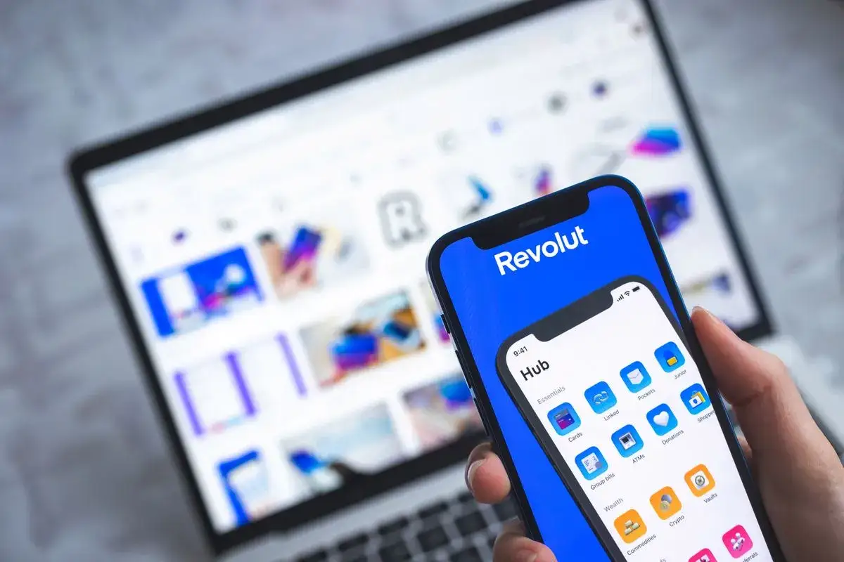 Dłoń trzyma smartfon z aplikacją Revolut, na ekranie laptopa widać interfejs tej samej aplikacji. Możliwość uzyskania kredytu w Revolut jest na wyciągnięcie ręki.