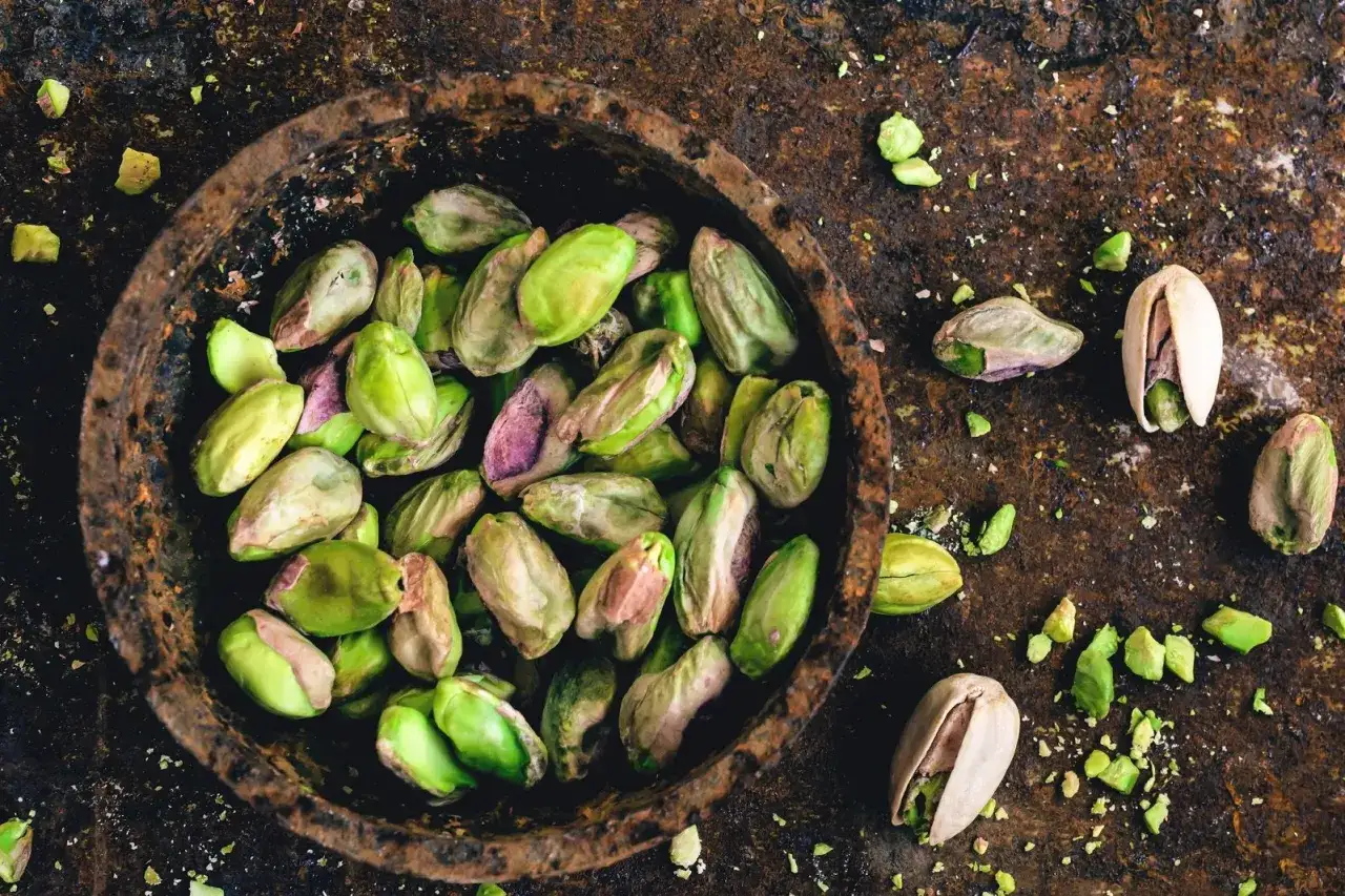 Pistacchi sgusciati in una ciotola rustica, con alcuni sparsi intorno. Scopri le incredibili propriet&agrave; dei pistacchi per la tua salute.