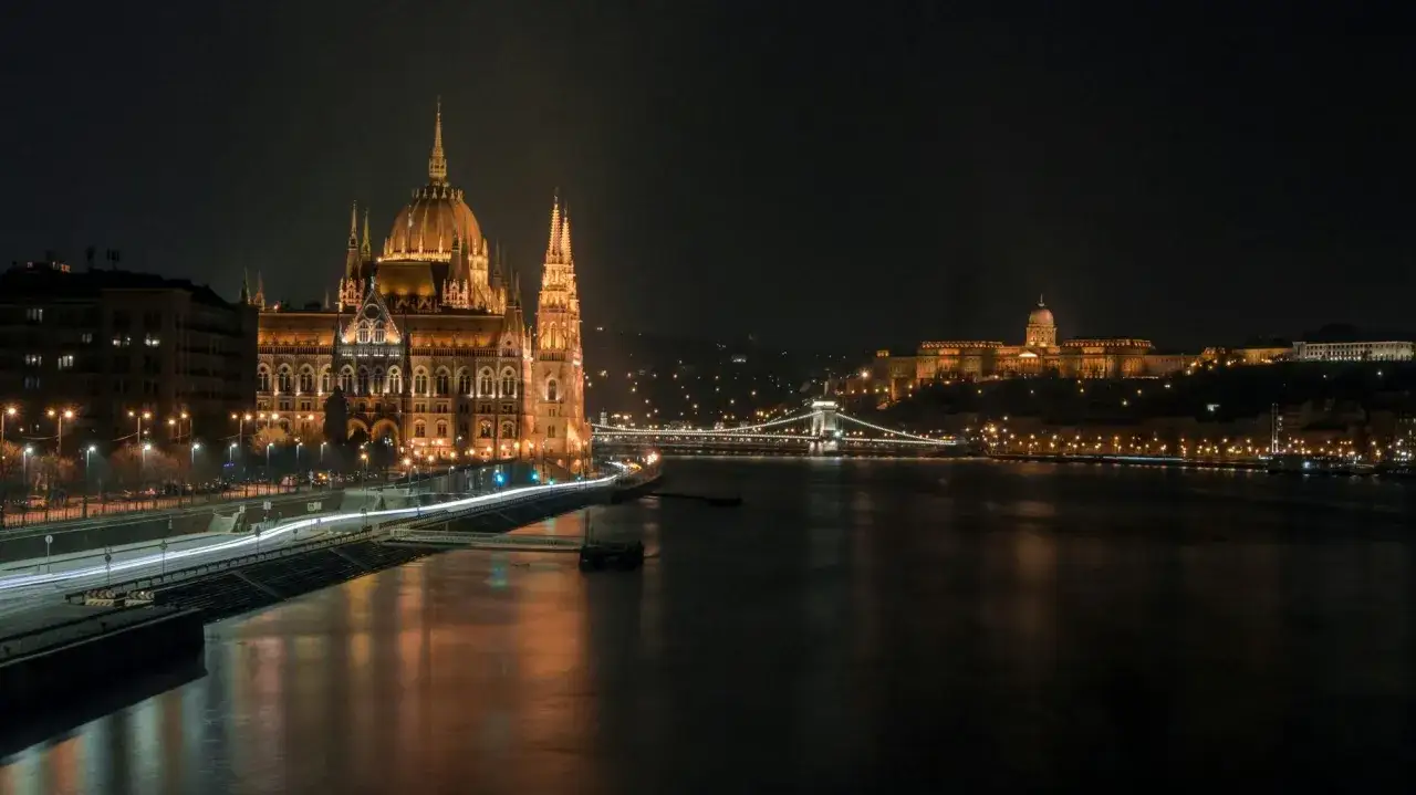 Budapeszt nocą, Parlament i Zamek Królewski nad rzeką Dunaj. Światła miasta odbijają się w wodzie.